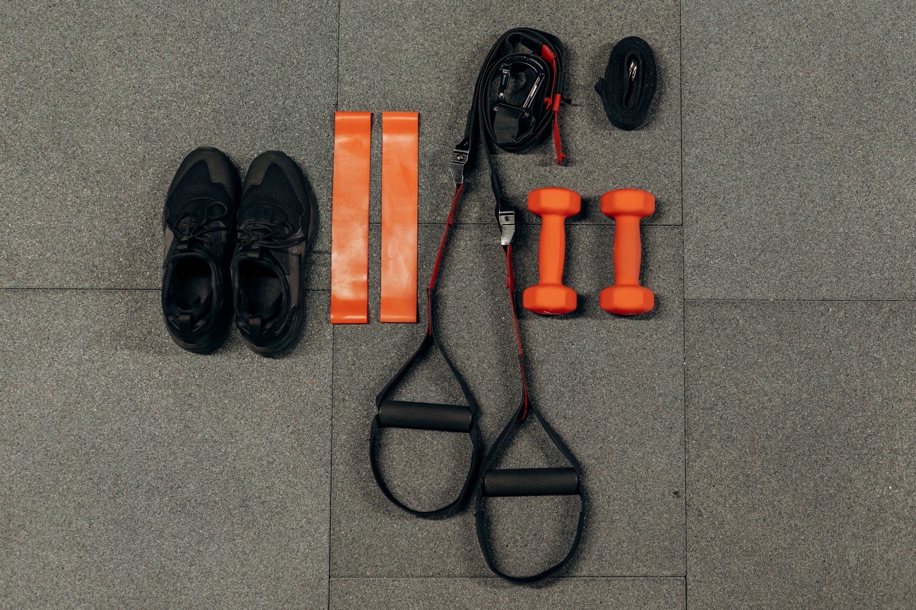 Resistance bands, dumbbells and suspension straps laid out on a gym floor